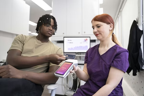 Patient paying at reception using a card on a handheld terminal held by a clinician in a bright clinical office