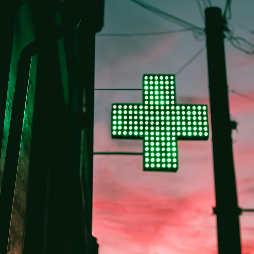Illuminated green medical cross sign at dusk